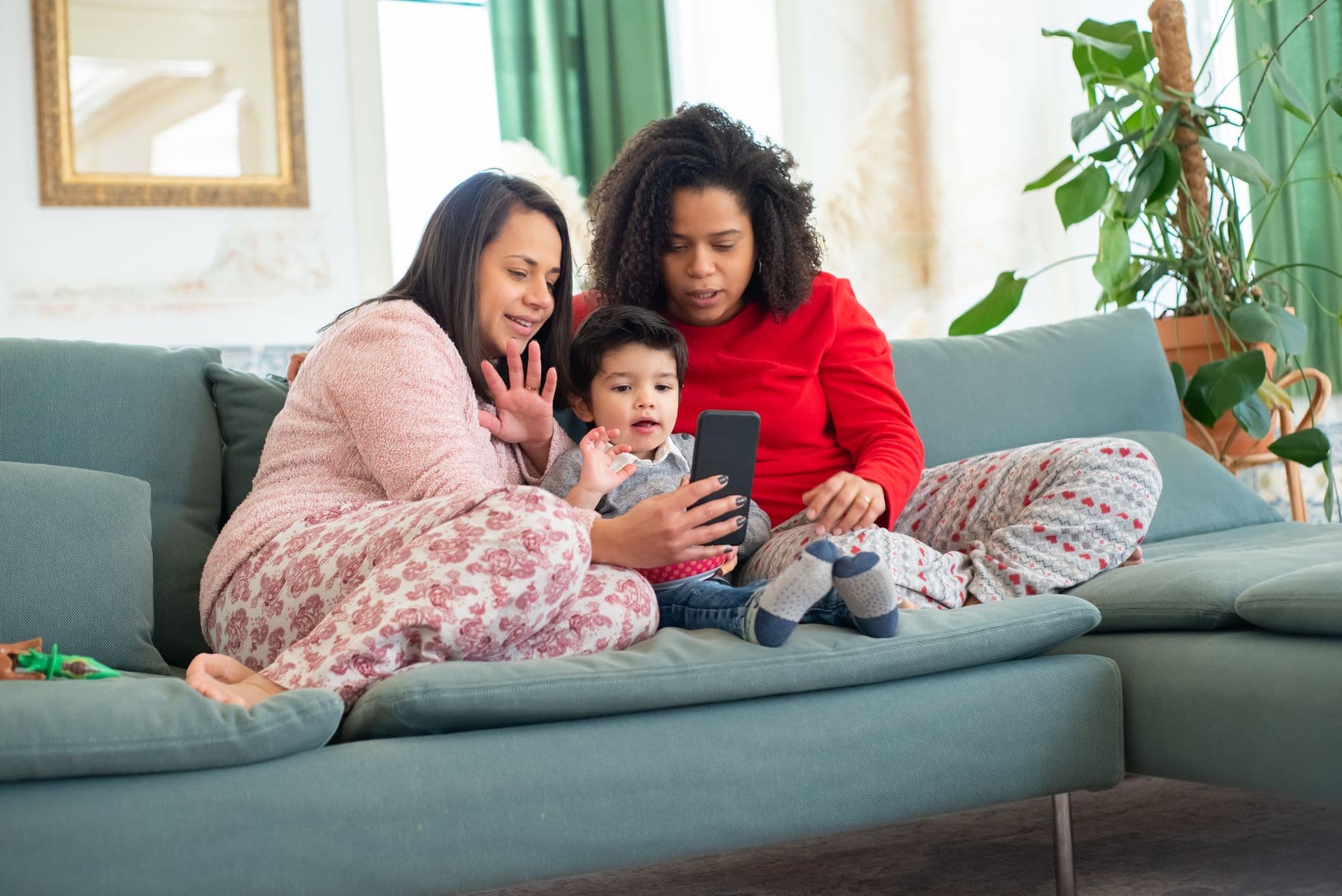 A family sitting together on the couch, parents and child looking at the same phone screen