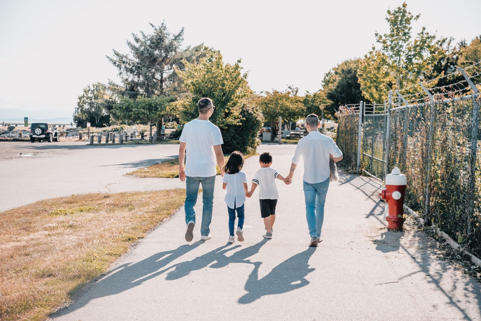 Parents walking down a leafy sidewalk holding their young child's hands