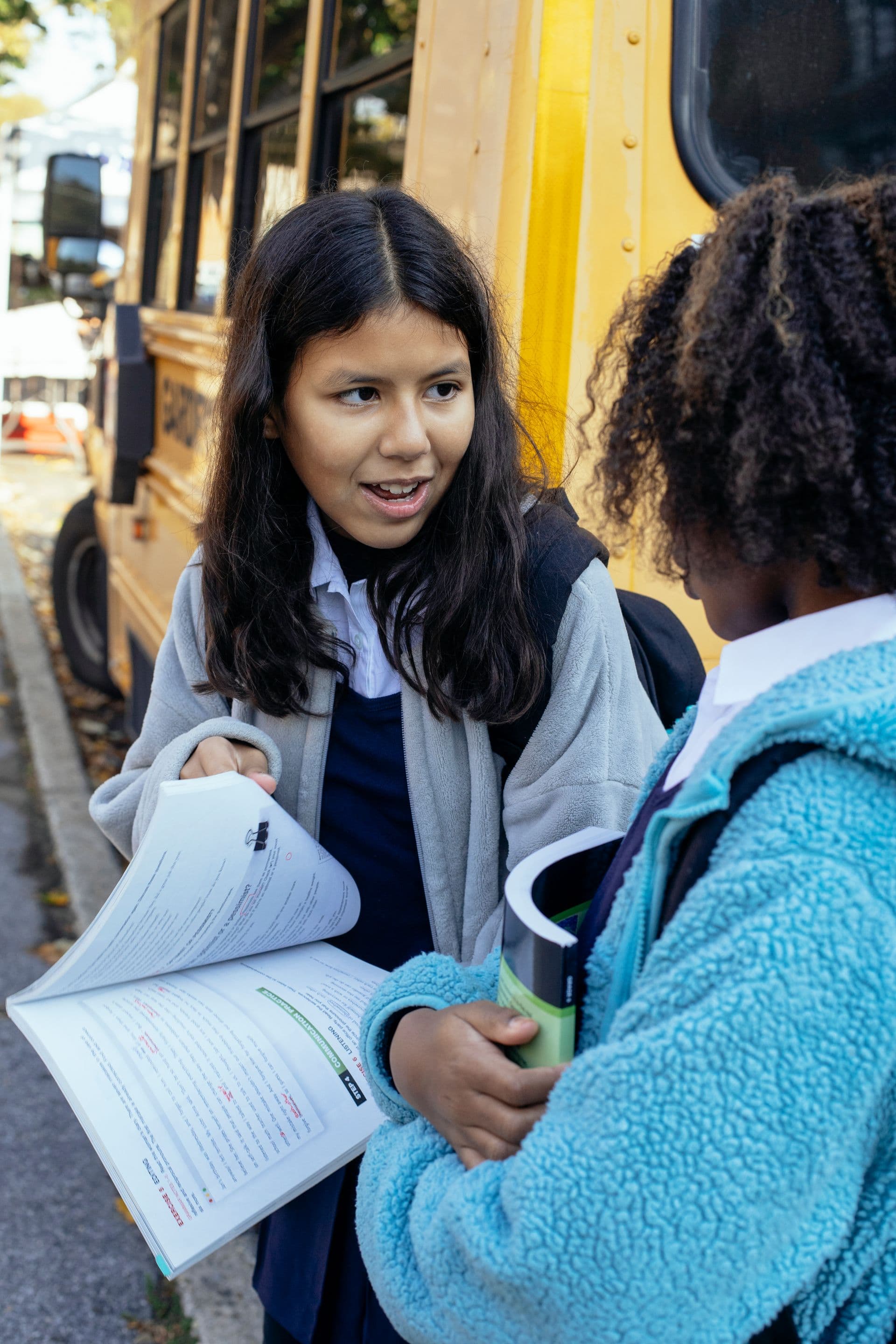 Two girls with backpacks talking outside a yellow school bus