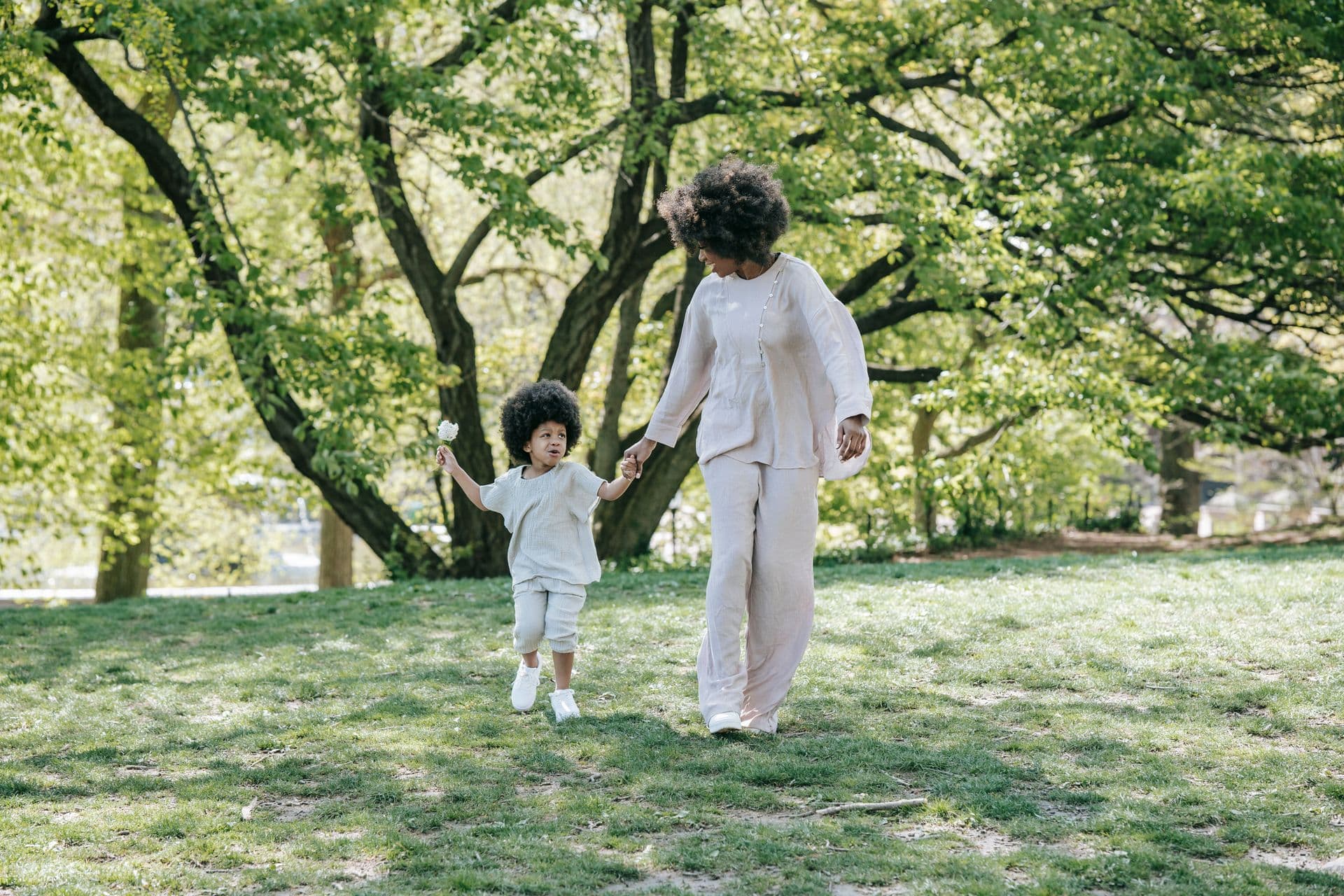 A mother kneeling in the park, laughing with her young child