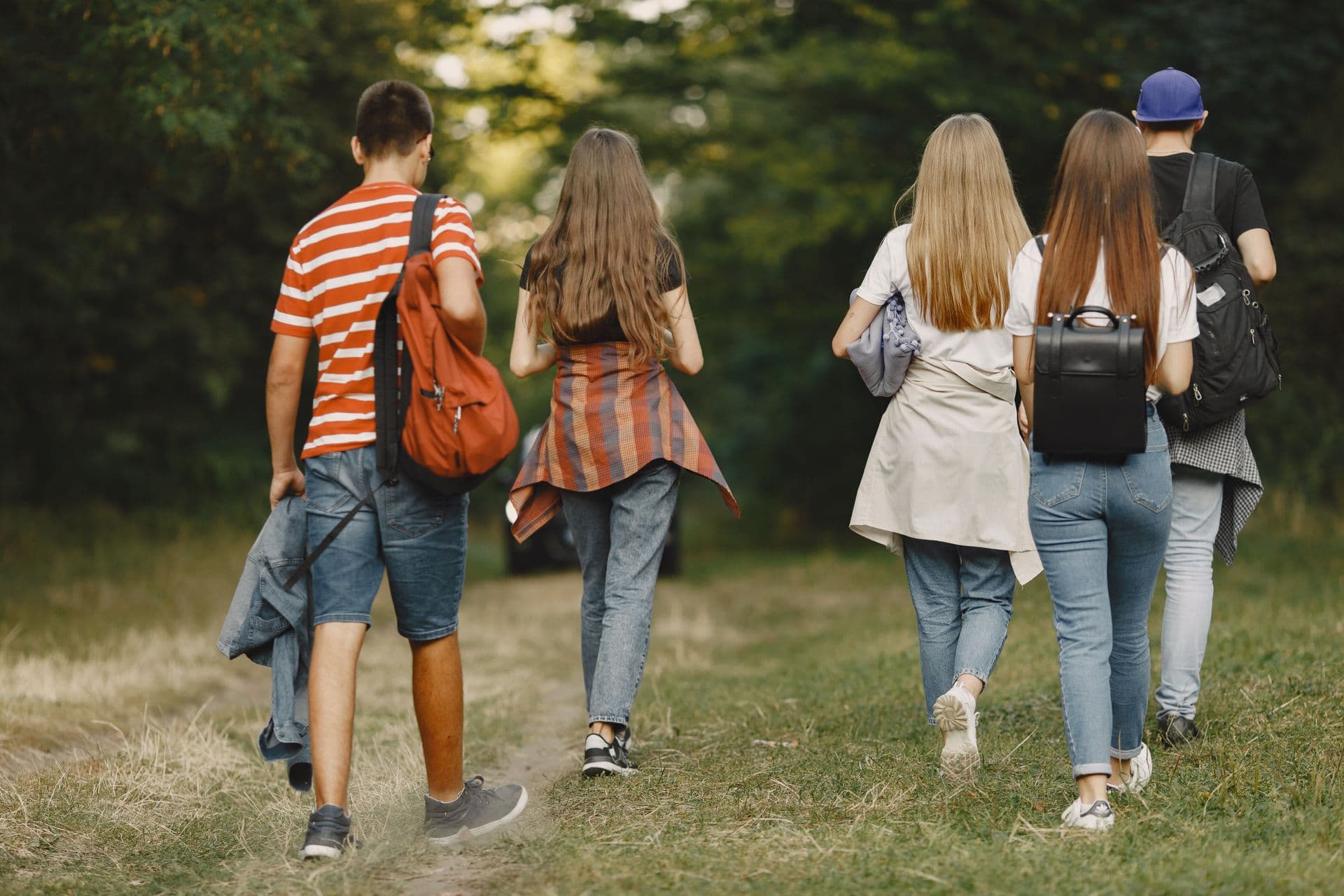 A group of teens with backpacks walking together along a wooded trail